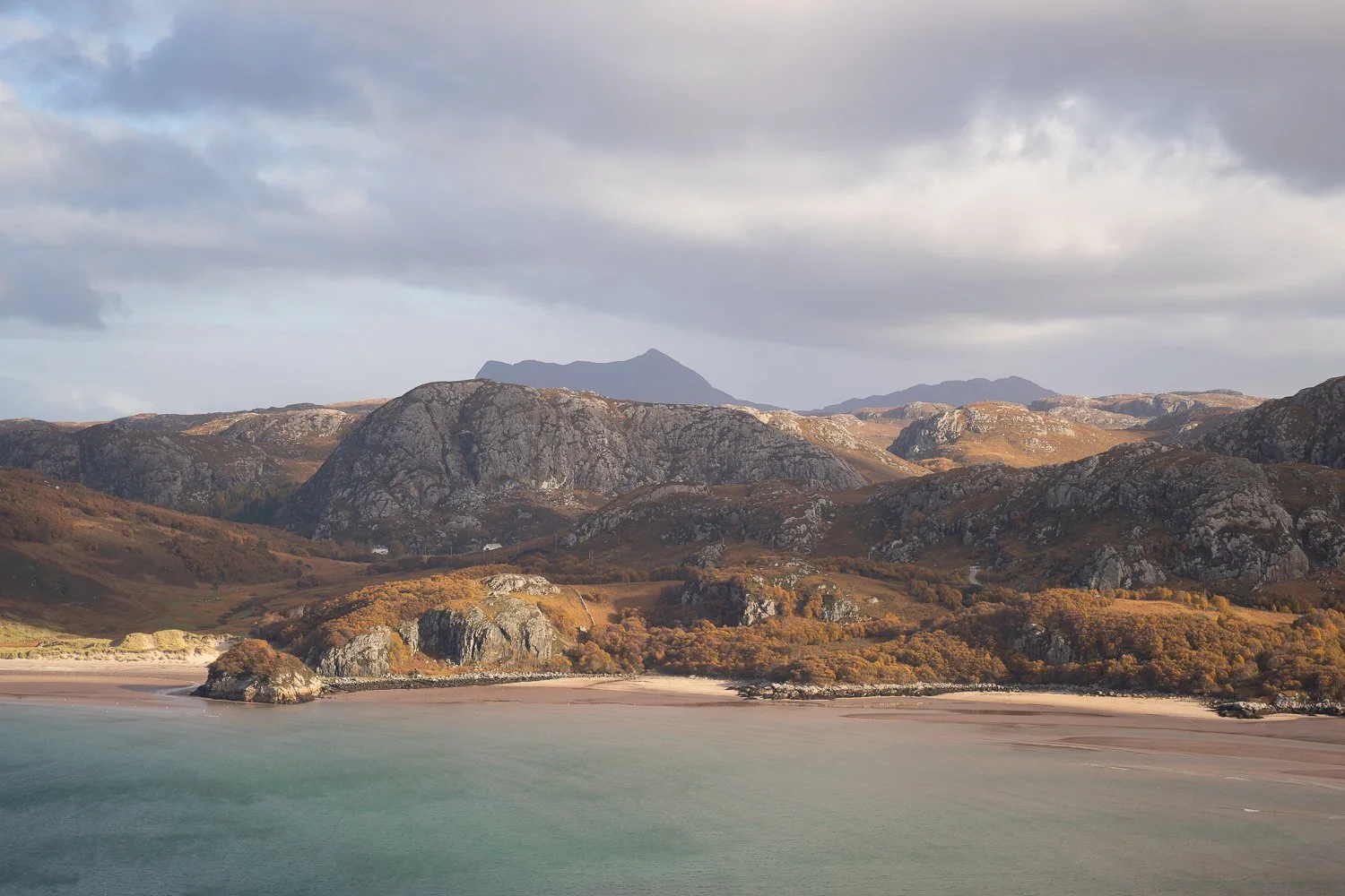 Gruinard Bay with turquoise water, sandy beach and Highland mountains during golden hour.