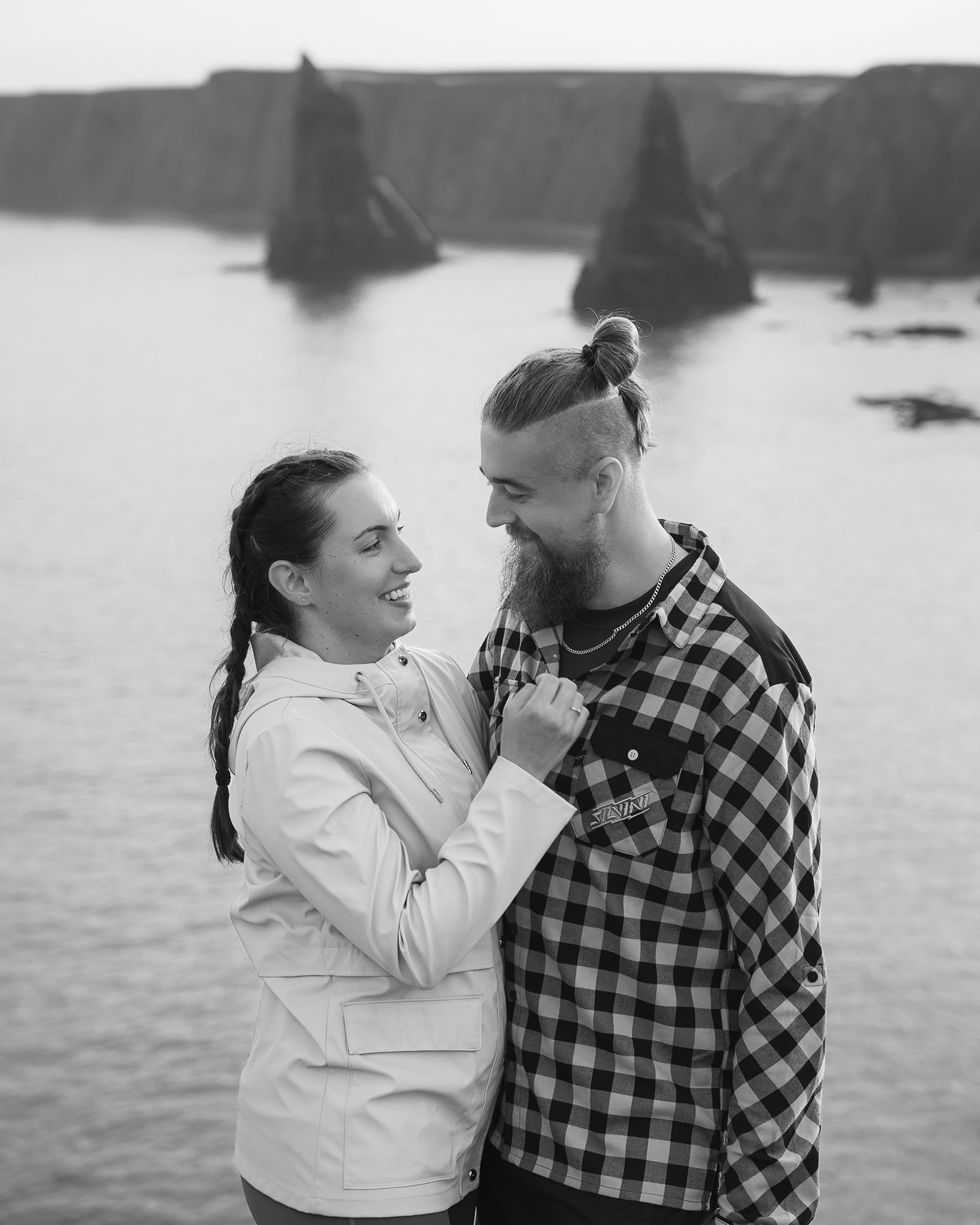 Smiling couple standing together with dramatic Duncansby Stacks rising from ocean creating stunning coastal backdrop.