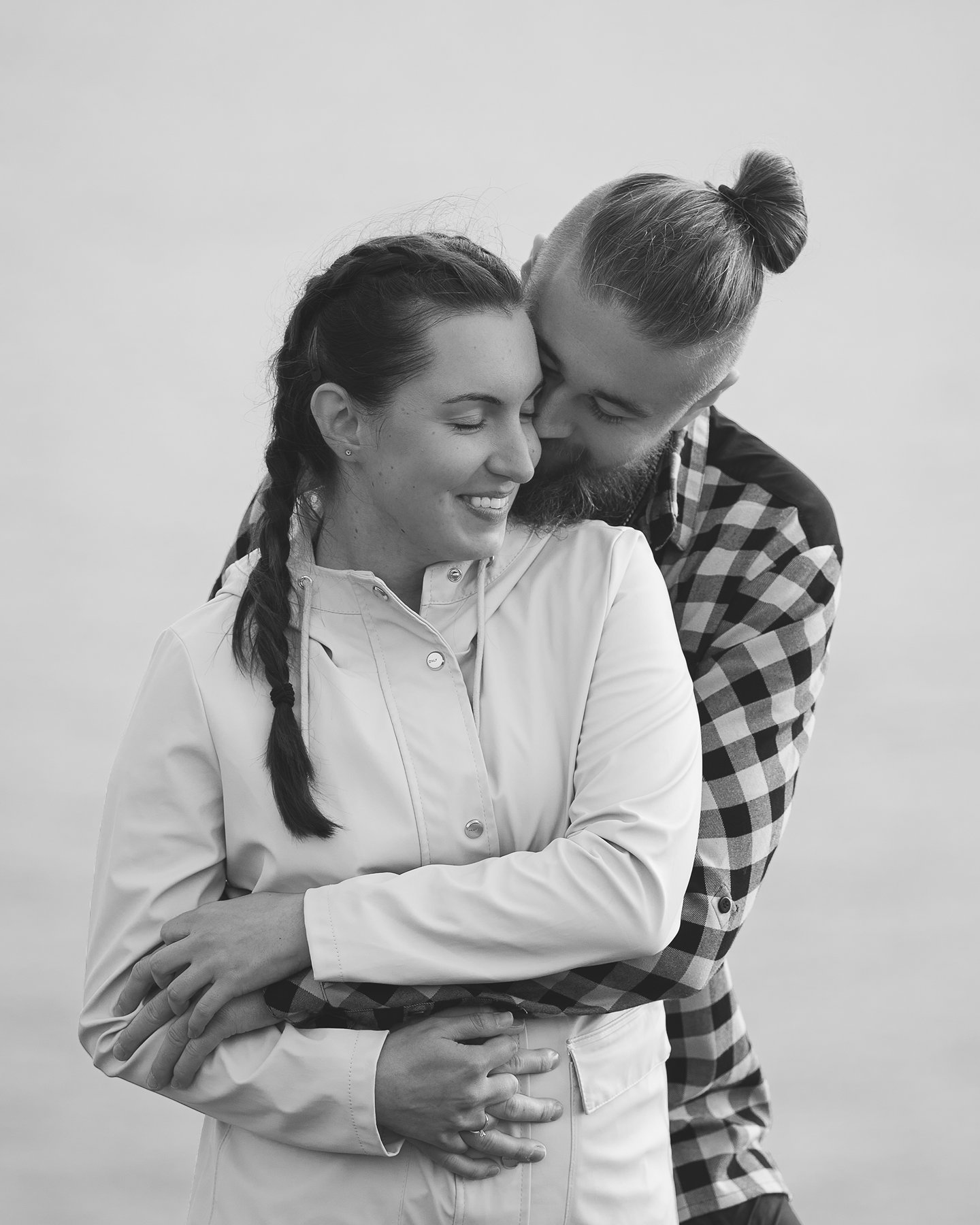 Couple embracing as man kisses woman’s cheek, she smiles with eyes closed in a tender, romantic moment.