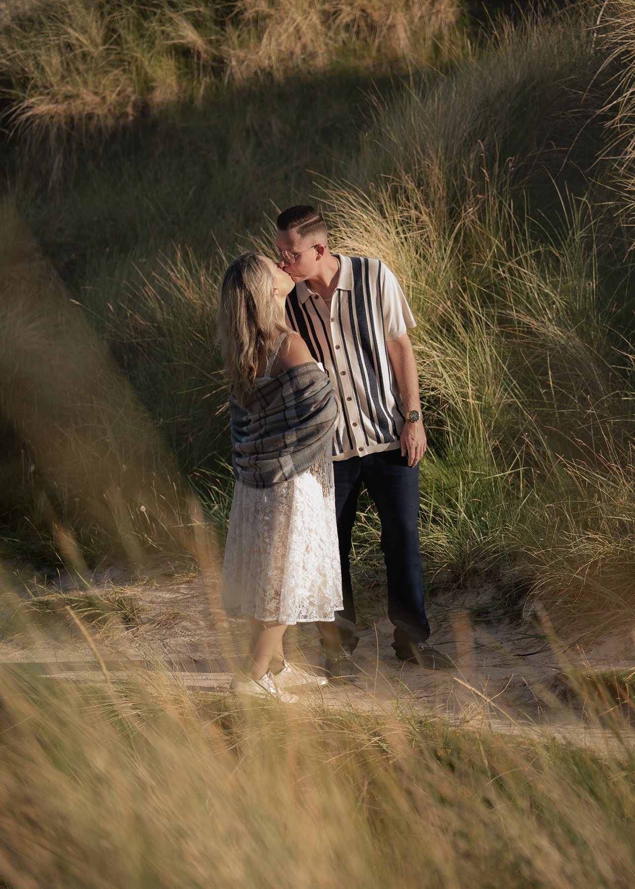Couple kissing among Highland dune grass during romantic engagement shoot