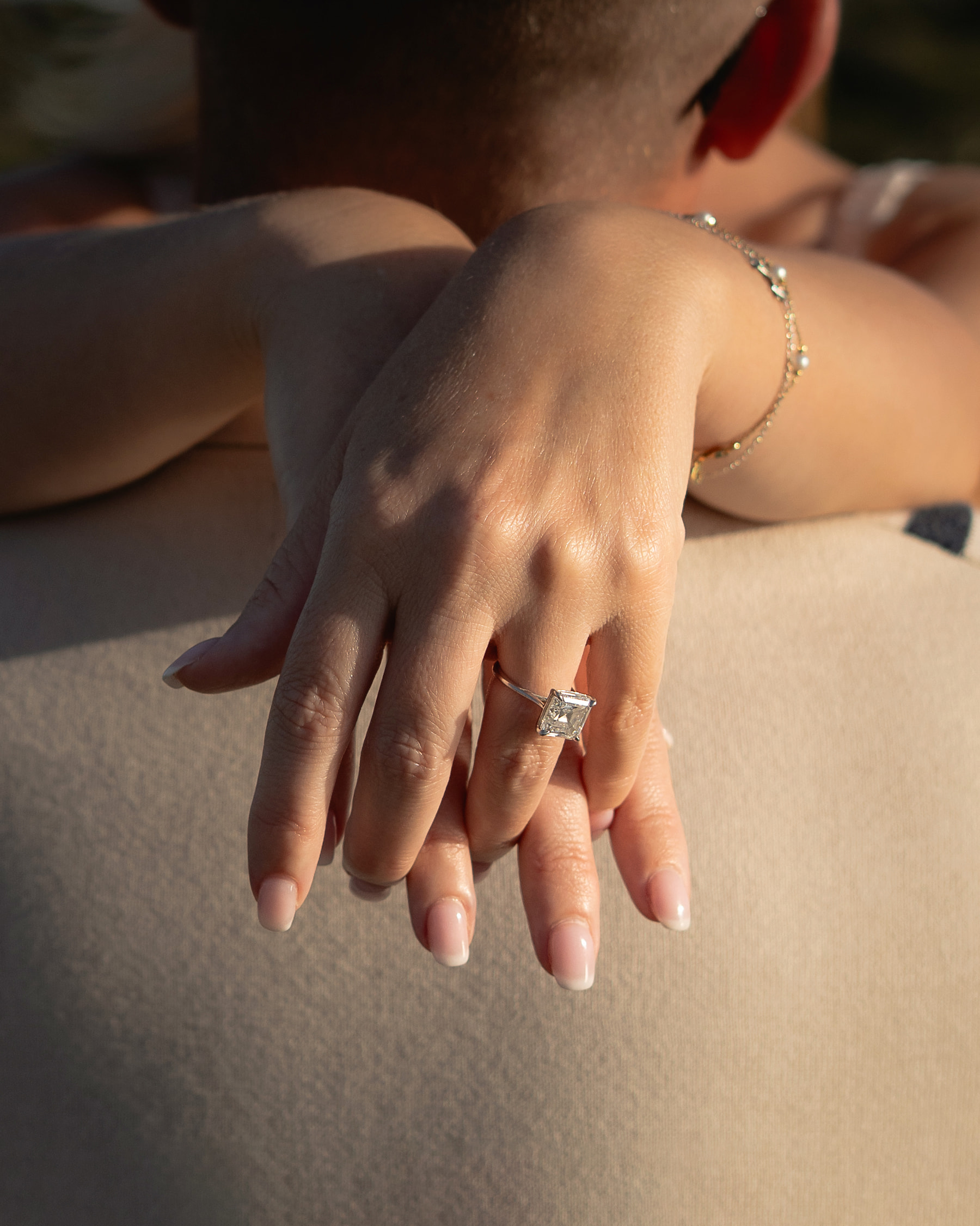 Elegant engagement ring shown on woman's hand as she touches her fiancé's shoulder.