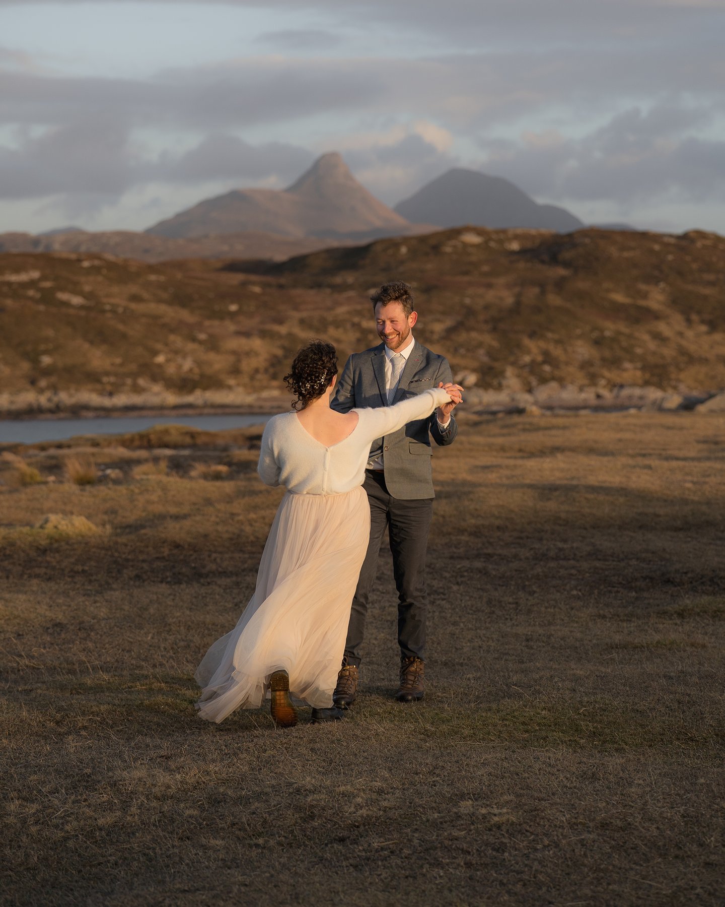 Elopement couple dancing on rugged Scottish landscape with mountains and loch in background.