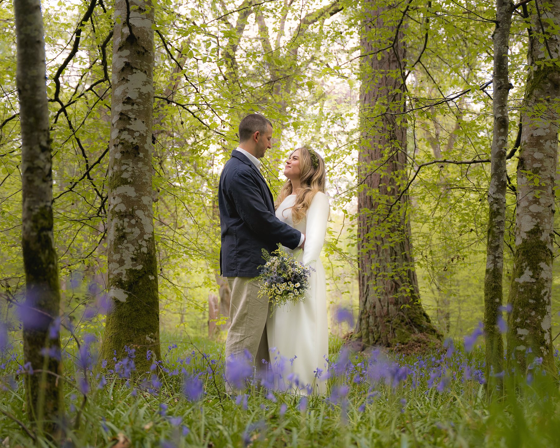 Wedding couple among spring bluebells in Scottish birch forest.